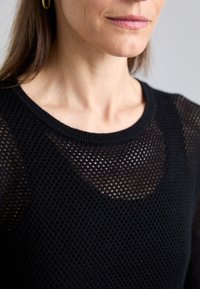 Maglione nero a maglia con texture a rete. Presenta un collo rotondo e un design attillato, mettendo in mostra un motivo a tessitura aperta.