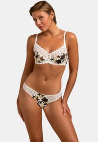Soutien-gorge en dentelle blanche et slip assorti avec un motif floral en beige, jaune et noir. Présente des bords en dentelle et des boutons décoratifs sur le soutien-gorge.