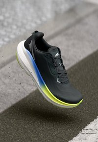 Chaussure de sport noire avec un dessus texturé, présentant des accents en dégradé bleu et vert sur la semelle et un logo distinctif sur le côté.