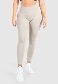Beige hoge taille leggings van ribbelstof, met een gladde textuur en een aansluitend ontwerp, gecombineerd met witte sportschoenen.