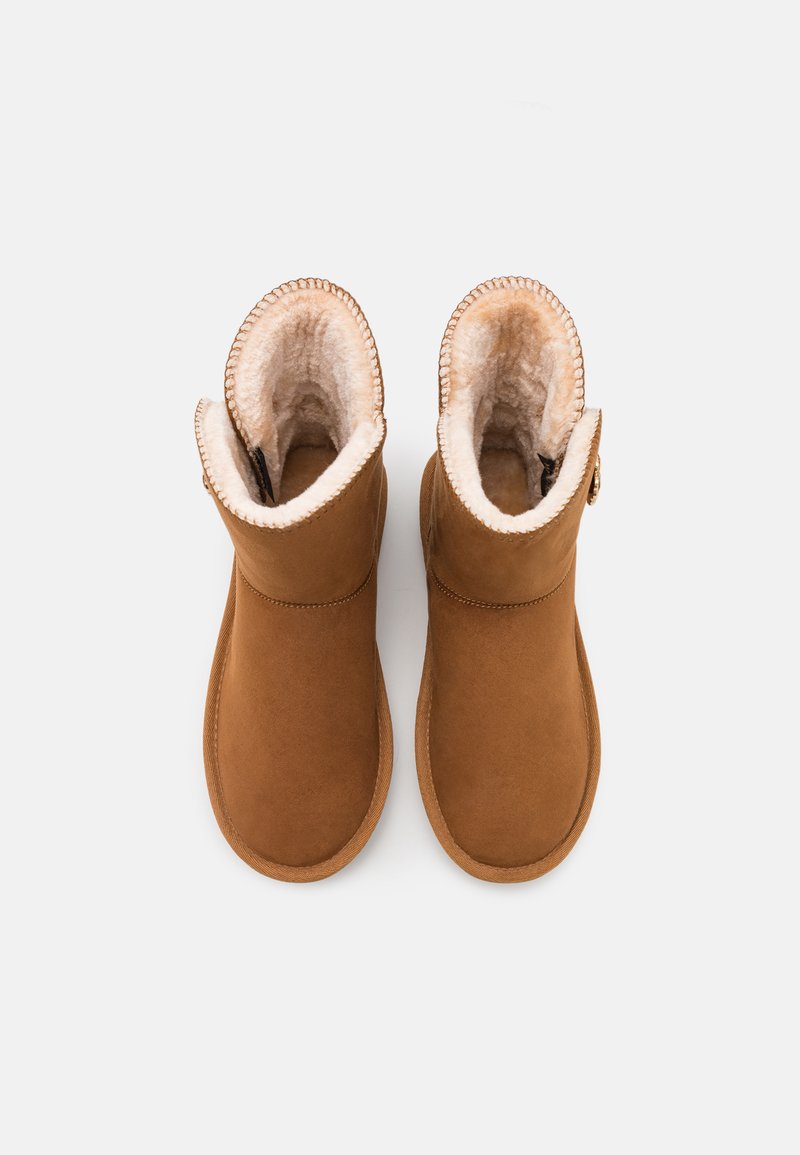 Braune falsche Wildleder-Ankle-Boots mit einem weichen, beigen Kunstpelzfutter, runder Zehenform und genähten Akzenten entlang des Schaftes und der Sohle.