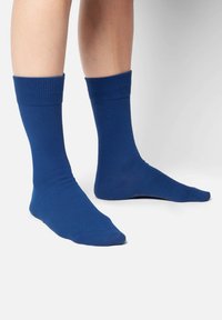 Blaue Baumwollsocken mit gerippten Bündchen, glatter Textur und flachen Zehennähten. Die Socken bedecken die Unterschenkel und sitzen gerade über dem Knöchel.