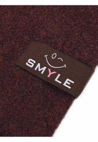 Burgunderfarbener Filzstoff mit einer strukturierten Oberfläche; versehen mit einem braunen Etikett mit weißem und rosafarbenem "SMYLE"-Text und einer lächelnden Gesichtsgrafik.