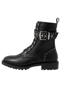 Bota de cuero negro hasta el tobillo con cordones en la parte frontal, acentos con tachuelas y un detalle de cinturón perforado. Tacón cuadrado y suela de goma texturizada.