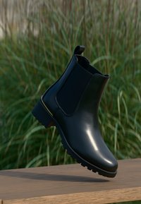 Černá kožená kotníková bota s elastickými bočními panely, texturovanou gumovou podrážkou a malým zlatým detailem u paty. Nízký úhel designu.