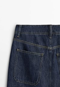 Vue arrière d'un jean denim bleu foncé montrant deux grandes poches arrière, des passants de ceinture et des surpiqûres diagonales sur le yoke.