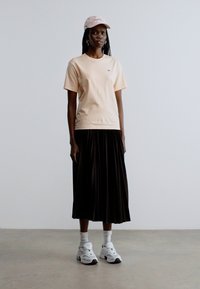 Lyse ferskenfarvet T-shirt med korte ærmer, sort plisseret nederdel, hvide sneakers og lyserød kasket. Simpelt design med en behagelig pasform og klassisk silhuet.