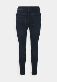 Tummansiniset skinny-farkut, joissa on kaksi takataskua ja huomaamaton ommel, esitelty takaa valkoista taustaa vasten.