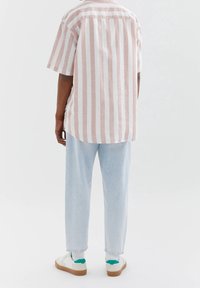 Gestreept shirt met korte mouwen in lichtroze en wit, met een afgeronde zoom. Gecombineerd met lichtblauwe broek en witte sneakers met groene accenten.