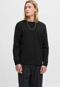 Schwarz langärmliges T-Shirt mit Rundhalsausschnitt, aus weichem Stoff gefertigt. Trägt zu einer gestreiften Hose. Zusätzliche Details umfassen eine silberne Kette.