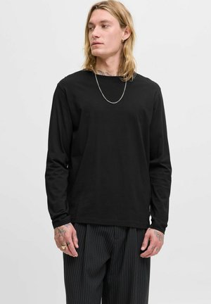 Langærmet sort t-shirt med rund hals, lavet af blødt stof. Bæres med stribede bukser. Yderligere detalje inkluderer en sølv kæde halskæde.