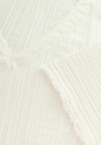 Fältiger Creme-Stoff mit weicher Textur, V-Ausschnitt-Design und rohen Kanten. Leicht und leicht durchsichtig.