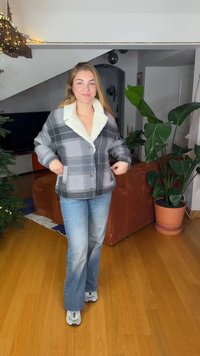 Veste à carreaux avec col sherpa crème, tons gris et noirs, fermeture à boutons et poignets élastiques. Portée avec un jean évasé bleu.