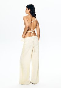 Ensemble en deux pièces de couleur crème clair, texturé, comprenant un haut sans dos avec des lanières et un pantalon à jambes larges, tous deux ornés de motifs en vagues subtils.