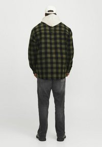 Groene en zwarte ruiten flanellen shirt met lange mouwen, relaxed fit, met een witte kap eronder en grijze jeans. Effen pet gedragen.