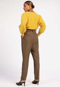 Geel donzig sweater met pofferige mouwen, bruine op maat gemaakte hoge taille broeken en zwarte hak sandalen met studs. Achteraanzicht.