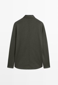 Camicia verde scuro a maniche lunghe con colletto, vista da dietro su uno sfondo bianco uniforme.