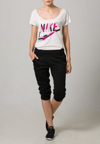 Camiseta blanca de manga corta con el logotipo de Nike en colores, combinada con pantalones deportivos negros de corte ajustado con puños elásticos y bolsillos laterales.