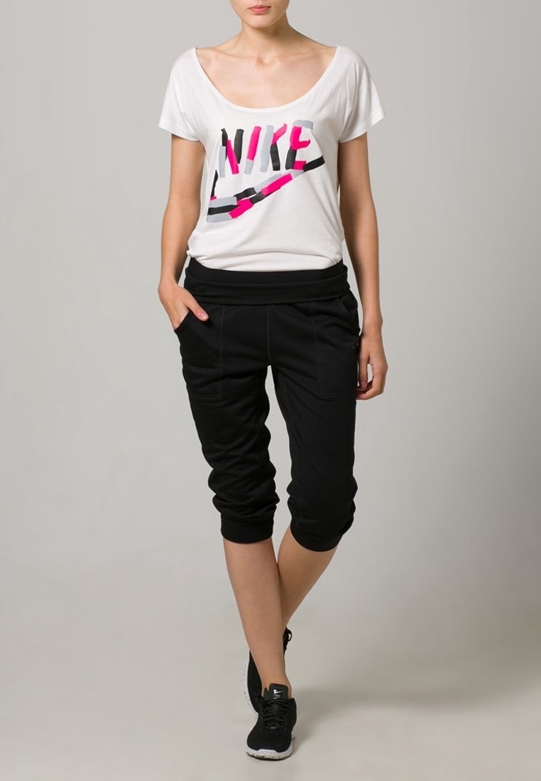 Camiseta blanca de manga corta con el logotipo de Nike en colores, combinada con pantalones deportivos negros de corte ajustado con puños elásticos y bolsillos laterales.