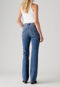 Vaqueros azules de talle alto hechos de mezclilla, con un diseño de pierna acampanada, bolsillos traseros con detalle de costura y una etiqueta de cuero marrón en la cintura.