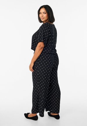 Black polka dot jumpsuit featuring short sleeves, a relaxed fit, and wide leg design. Soft fabric with a slightly textured surface.