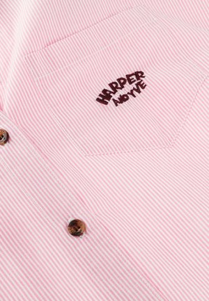 Tissu à rayures roses et blanches avec une poche poitrine brodée de "HARPER AND YVE" et deux boutons marron en dessous de la poche.