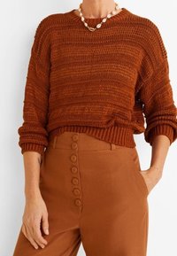 Sweter z dzianiny w kolorze rdzy z teksturowanymi paskami, okrągłym dekoltem i opuszczonymi ramionami, zestawiony z wysokim stanem i spodniami z guzikiem z przodu w dopasowanym odcieniu.