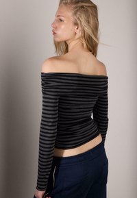 Top a righe nere e grigie con scollo a barca e maniche lunghe, caratterizzato da un design aderente e una texture a coste, abbinato a pantaloni blu navy.