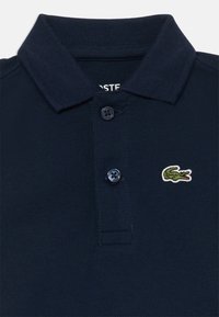 Mornarica polo majica iz teksturirane tkanine, s trokrakim patentom, dvema tamnima dugmadi i malim zelenim krokodilom logotipom na prsima.