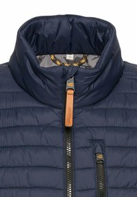 Marineblaue Pufferjacke mit hohem Kragen, horizontaler Steppung, Frontreißverschluss und kontrastierenden Reißverschlussakzenten. Größenetikett sichtbar.