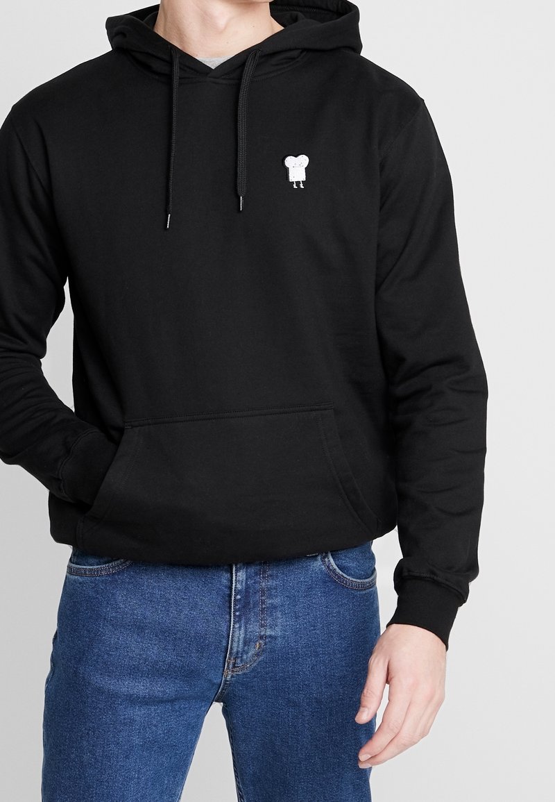 Felpa nera con cappuccio realizzata in materiale morbido, dotata di tasca frontale e coulisse. Piccola applicazione di un personaggio bianco sul petto. Vestibilità classica.
