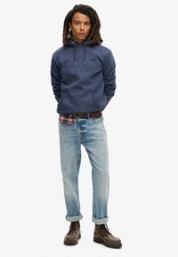 Felpa blu navy con tasca frontale, maniche lunghe e coulisse regolabile, abbinata a jeans azzurri strappati e stivali marroni.