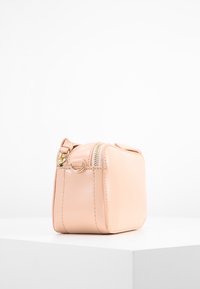 Ljusrosa rektangulär handväska gjord av slät konstläder. Har en dragkedjeslutning upptill och ett litet ögla-handtag på sidan.