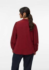 Bordeauxblouse met poefmouwen, met kantaccenten bij de manchetten. Gemaakt van lichtgewicht stof, ontworpen met een klassieke kraag.