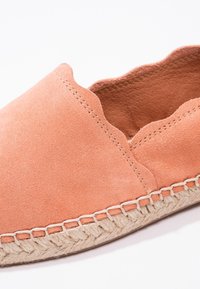 Espadrilles en suédine corail avec un bord festonné, dotées d'une semelle en jute tissée et de coutures visibles le long du dessous. Texture douce, design décontracté.