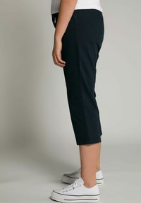 Donkerblauwe cropped broek met een gladde textuur, voorzien van een zijrits en een rechte snit, gecombineerd met witte canvas sneakers.