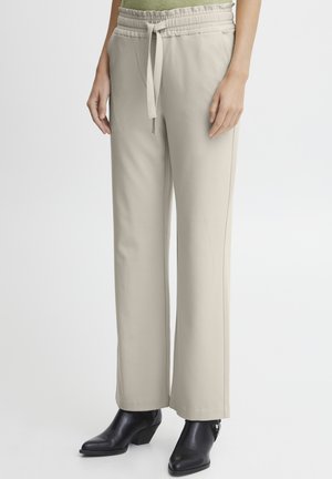 Beige wijde broek met een elastische tailleband en trekkoord. Zachte stof met zijzakken, gecombineerd met zwarte enkellaarsjes met hak.