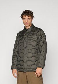 Chaqueta acolchada en verde oliva oscuro, con un patrón de olas, botones a presión y una textura ligera. Diseñada con un cuello con solapa.