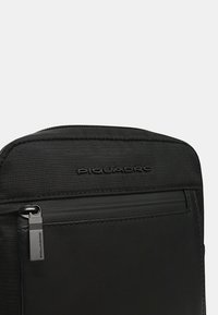 Borsa Piquadro nera realizzata in tessuto resistente, con una tasca con cerniera e una finitura strutturata. Include un piccolo dettaglio in metallo.