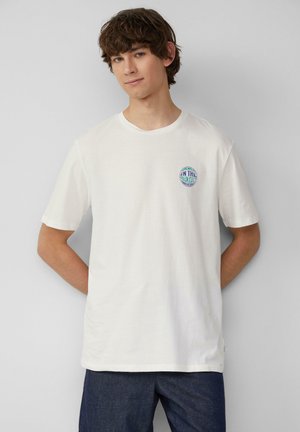 T-shirt en coton blanc avec un col rond et des manches courtes, arborant un graphique circulaire coloré sur la poitrine gauche.
