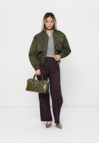 Maslinasto zelena bomber jakna s dva prednja džepa, sivi skraćeni top, tamnoljubičaste široke hlače i sjajna zelena torba s detaljem u obliku zvjezdice.