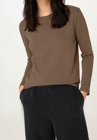 Haut marron à manches longues avec un col rond, fabriqué en tissu doux. Associé à un pantalon noir ample avec des poches latérales.