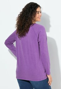 Fialová dlouhá halenka z měkké tkaniny, s volnějším střihem, zaobleným lemem a raglánovými rukávy.