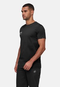 Svart bomullströja med rundad hals, korta ärmar och subtilt tryck på bröstet. Har en liten logotypdetalj på ärmen.