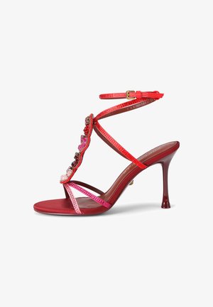 Sandalo rosso con tacco alto, cinturini sottili, fibbia alla caviglia e pietre decorative multicolori lungo il cinturino frontale.