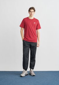 Red cotton t-shirt with short sleeves and a white logo, paired with black synthetic jogger pants. Footwear features gray sneakers.