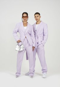 Lavadni srajčni sakoi z ujemajočimi se hlačami. Ženski outfit vsebuje srebrno torbico, medtem ko oba nosita bele čevlje. Gladka tekstura, sodoben dizajn.