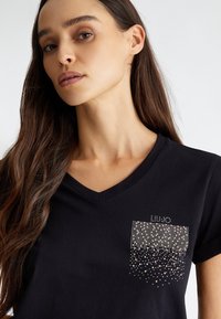 T-shirt nera a V, realizzata in cotone, con un design a tasca decorato da un motivo a gradient di borchie metalliche.