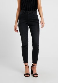 Svarta denim skinny-jeans med hög midja, utrustad med en standard knappstängning, fem fickor och en lätt fransad fåll.