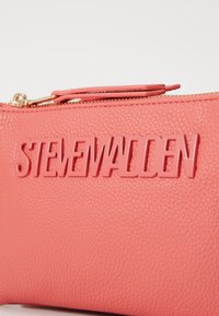 Coral textured leather pouch with a gold zip, featuring raised lettering "STEVENMADDEN" on the front.